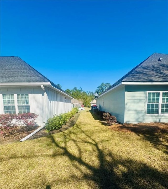 view of side of home featuring a yard and roof with shingles