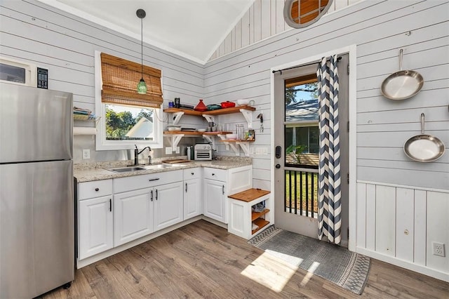 kitchen with white cabinets, wooden walls, pendant lighting, and stainless steel refrigerator