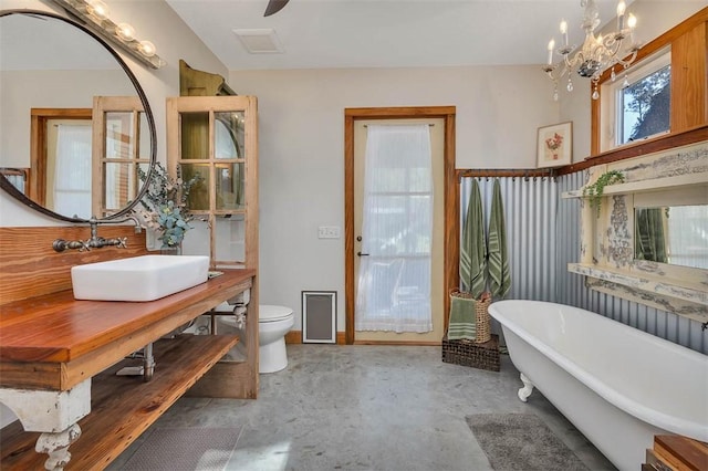 bathroom with a bath, an inviting chandelier, sink, toilet, and concrete floors