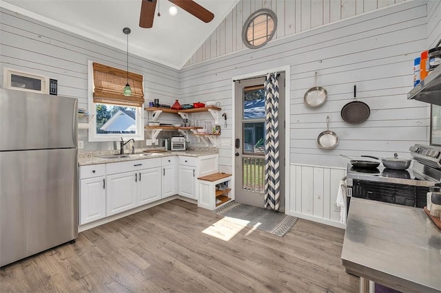 kitchen with wood walls, sink, hanging light fixtures, white cabinetry, and stainless steel appliances