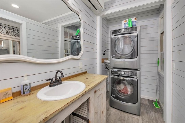 clothes washing area featuring wooden walls, stacked washer and dryer, wood-type flooring, and sink