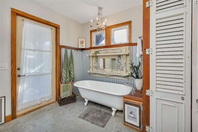 bathroom with concrete flooring, a bathtub, and a notable chandelier