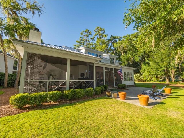 904 Champney, Saint Simons Island, GA 31522 - back of property featuring a sunroom, a chimney, a lawn, a patio, and a metal roof