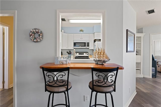 kitchen with stove, wooden counters, white cabinets, a kitchen breakfast bar, and dark hardwood / wood-style floors