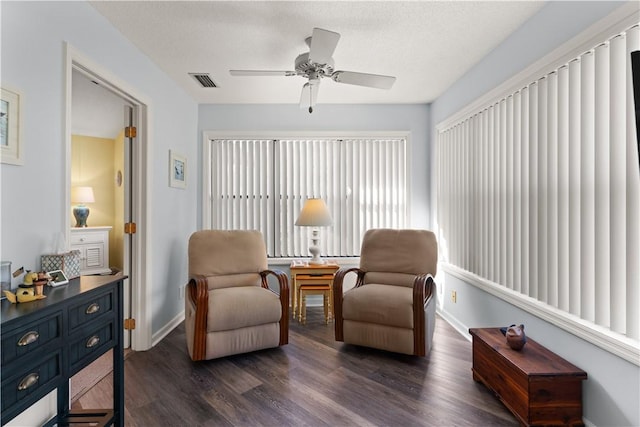 living area with ceiling fan, dark wood-type flooring, and a textured ceiling