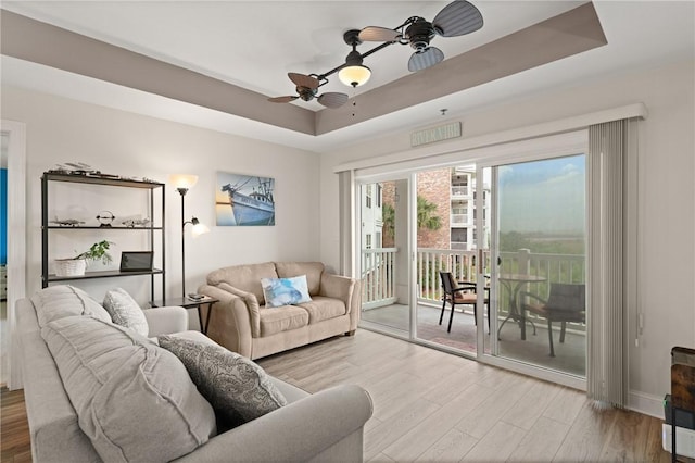 living room with a tray ceiling, wood finished floors, and ceiling fan