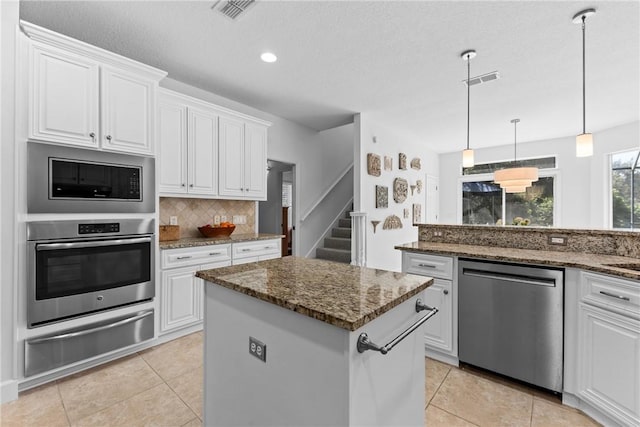 kitchen with stainless steel appliances, white cabinetry, a kitchen island, and dark stone countertops