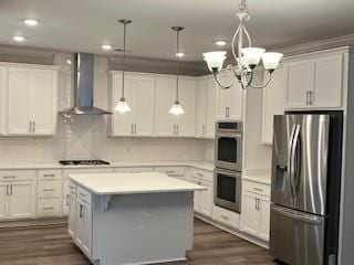 kitchen featuring appliances with stainless steel finishes, white cabinetry, a kitchen island, and wall chimney range hood