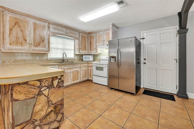 kitchen with light brown cabinets, white appliances, sink, light tile patterned floors, and a textured ceiling