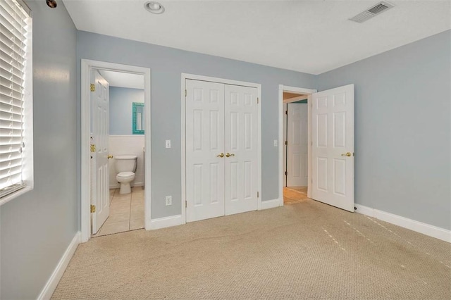 unfurnished bedroom with ensuite bathroom, a closet, and light colored carpet