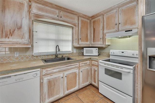 kitchen featuring tasteful backsplash, white appliances, sink, light tile patterned floors, and tile counters