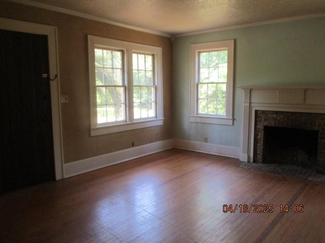 unfurnished living room with a textured ceiling, baseboards, wood finished floors, ornamental molding, and a high end fireplace