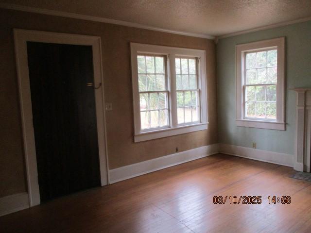 unfurnished room with plenty of natural light, wood finished floors, a textured ceiling, and crown molding