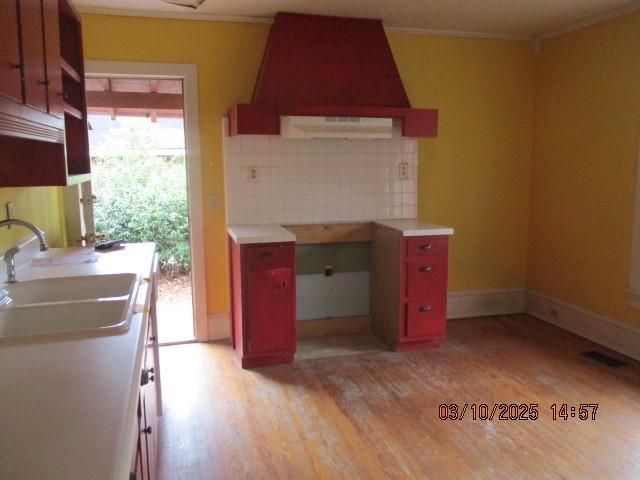 kitchen featuring backsplash, light countertops, a sink, light wood-style flooring, and custom range hood