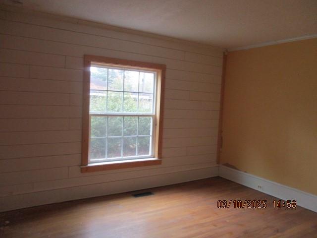 unfurnished room featuring wooden walls, wood finished floors, a healthy amount of sunlight, and baseboards