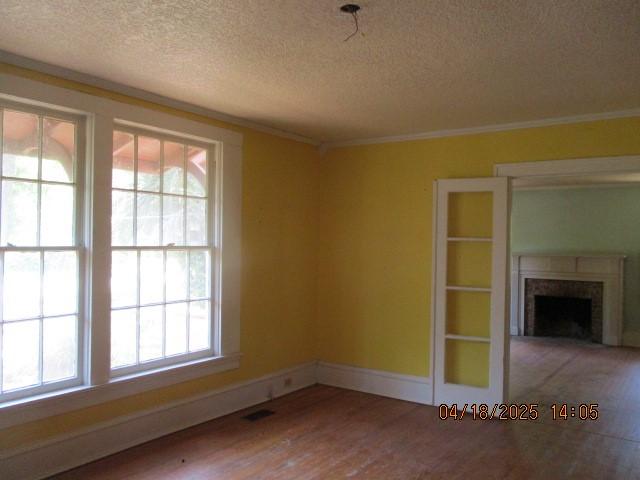 spare room featuring wood finished floors, a textured ceiling, visible vents, and a fireplace