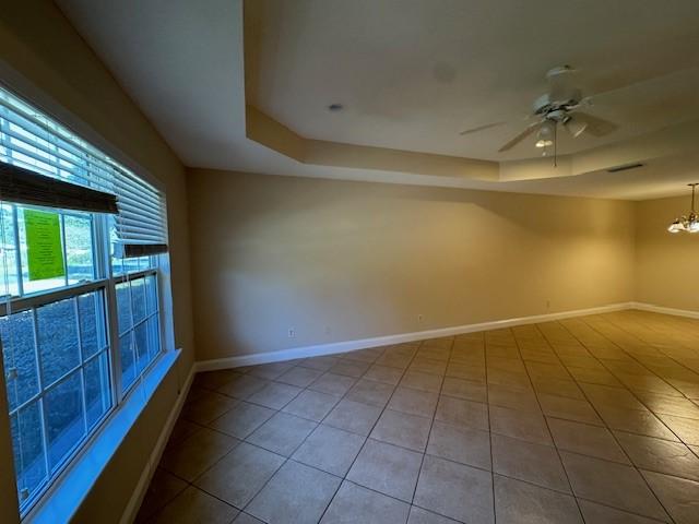 tiled empty room featuring ceiling fan with notable chandelier and a raised ceiling