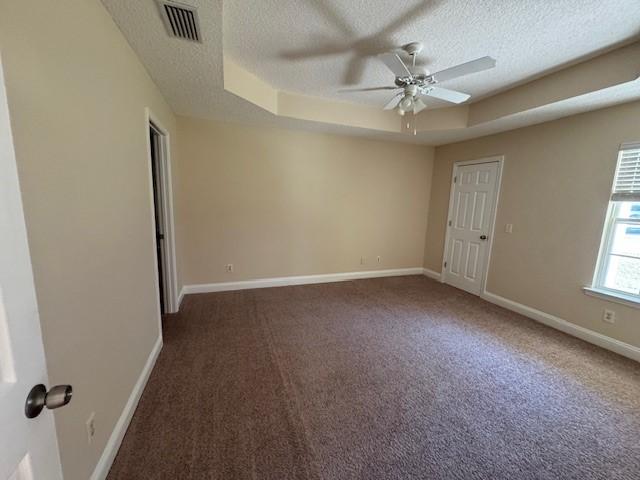 carpeted empty room featuring a raised ceiling, ceiling fan, and a textured ceiling