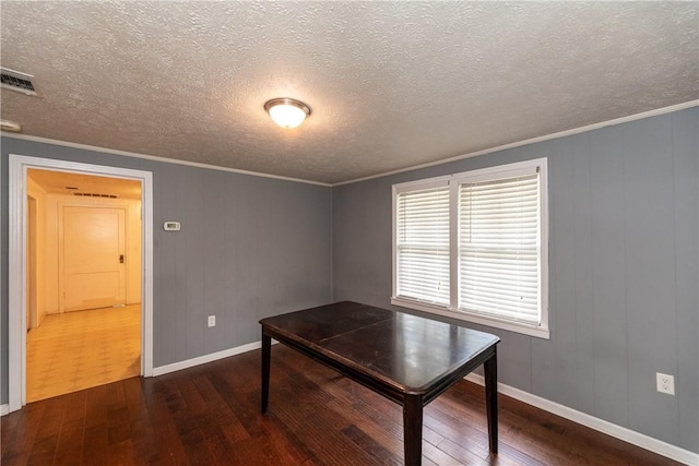 unfurnished dining area with dark wood-style flooring, visible vents, ornamental molding, a textured ceiling, and baseboards