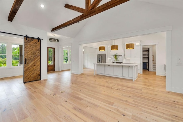 128 W Point Pkwy, Saint Simons Island, GA 31522 - unfurnished living room featuring a barn door, beamed ceiling, light wood-style floors, baseboards, and high vaulted ceiling
