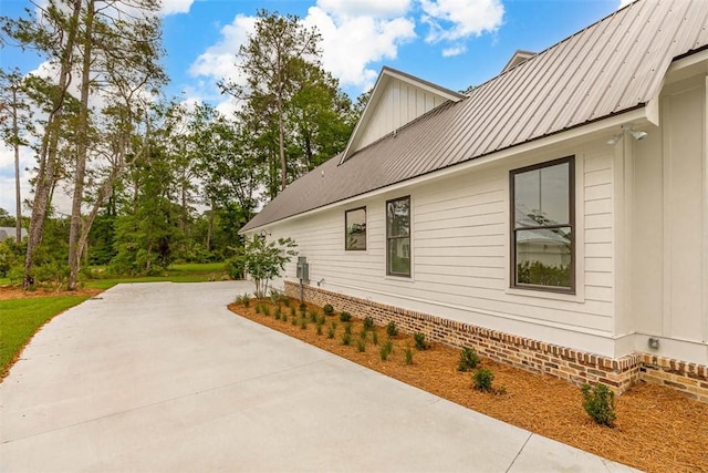 128 W Point Pkwy, Saint Simons Island, GA 31522 - view of home's exterior with board and batten siding, concrete driveway, metal roof, and a patio area