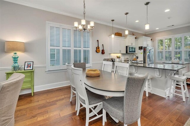 dining room with dark hardwood / wood-style flooring, ornamental molding, sink, and a chandelier