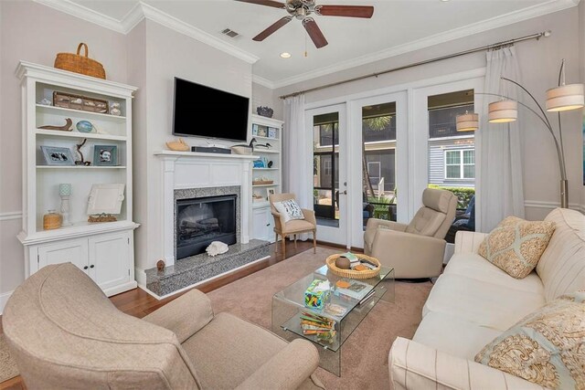 living room with ornamental molding, built in shelves, ceiling fan, wood-type flooring, and a fireplace