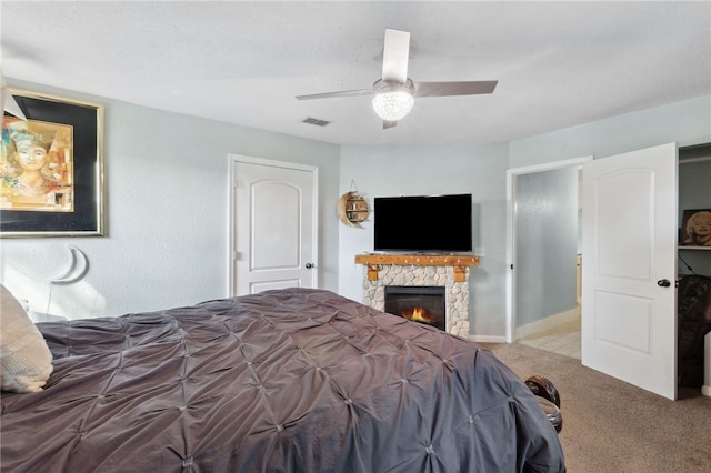 bedroom with carpet, visible vents, ceiling fan, and a stone fireplace