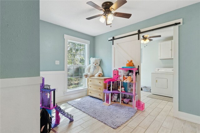 playroom with washer / dryer, a barn door, ceiling fan, and wood finished floors