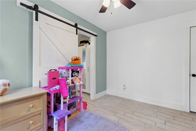 recreation room featuring light wood finished floors, a barn door, baseboards, and ceiling fan
