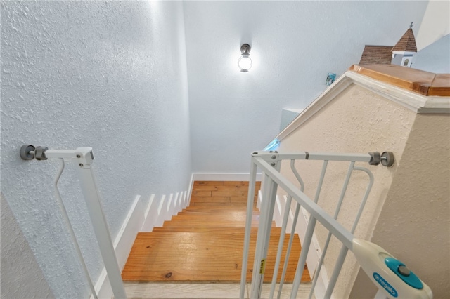 stairs with baseboards, wood finished floors, and a textured wall