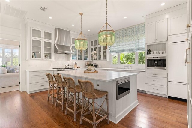 kitchen featuring plenty of natural light, a kitchen island, wall chimney range hood, and appliances with stainless steel finishes