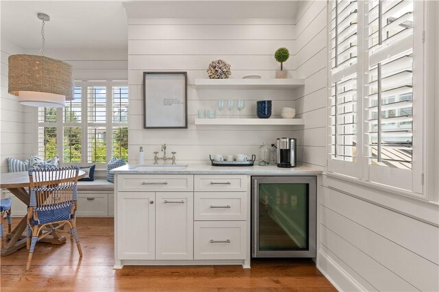 bar with wood walls, white cabinets, hanging light fixtures, wine cooler, and hardwood / wood-style flooring