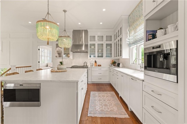 kitchen with appliances with stainless steel finishes, white cabinetry, a kitchen island, and wall chimney range hood