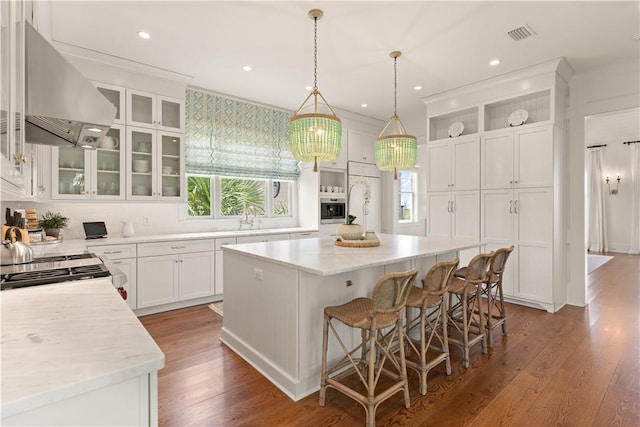 kitchen with dark wood-type flooring, a kitchen island, a breakfast bar area, white cabinets, and exhaust hood