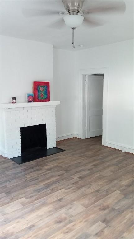 unfurnished living room featuring wood-type flooring, a brick fireplace, and ceiling fan