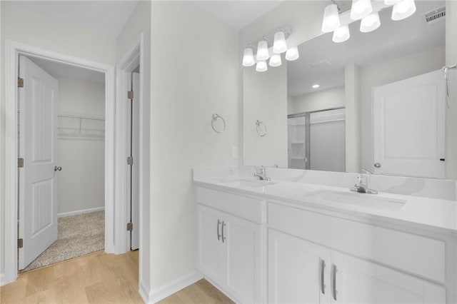 11026 Woodland Trl, Brunswick, GA 31525 - bathroom featuring wood finished floors, a stall shower, double vanity, a walk in closet, and baseboards