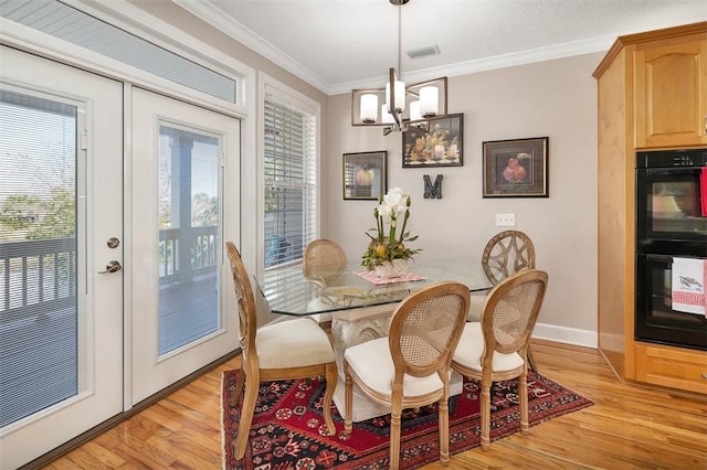 dining area featuring a notable chandelier, light wood-type flooring, ornamental molding, and french doors