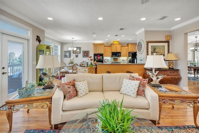 living room featuring a textured ceiling, a notable chandelier, crown molding, and light hardwood / wood-style flooring