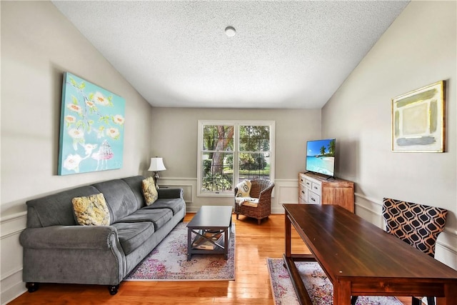 living room featuring lofted ceiling, wood-type flooring, and a textured ceiling