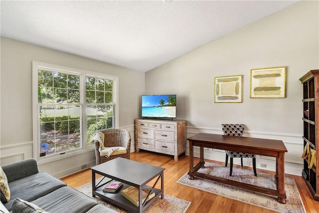 living room with a textured ceiling, light wood-type flooring, and vaulted ceiling