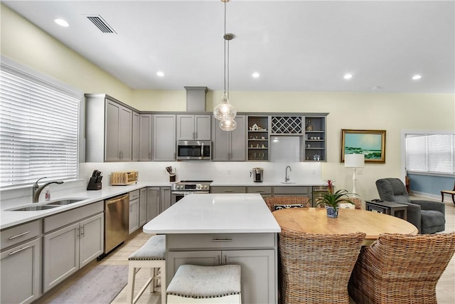 kitchen with appliances with stainless steel finishes, light hardwood / wood-style floors, sink, decorative light fixtures, and gray cabinets