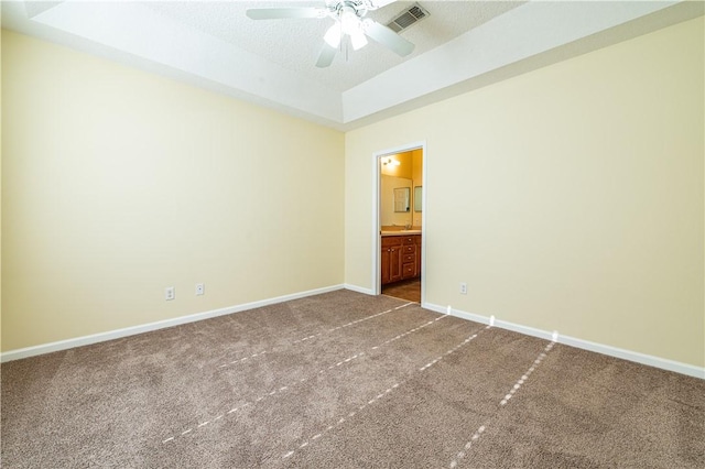 unfurnished bedroom featuring ensuite bathroom, carpet, ceiling fan, a tray ceiling, and a textured ceiling