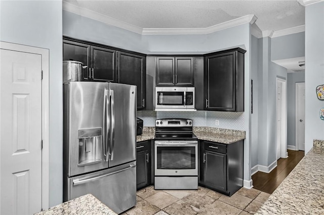 326 Daniel Trent Way, Kingsland, GA 31548 - kitchen featuring appliances with stainless steel finishes, dark cabinets, ornamental molding, light stone counters, and decorative backsplash
