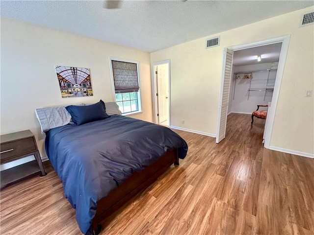 bedroom with a textured ceiling, baseboards, visible vents, a walk in closet, and light wood-type flooring