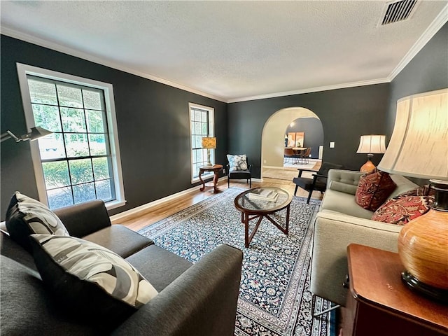 living area with arched walkways, ornamental molding, a textured ceiling, and wood finished floors
