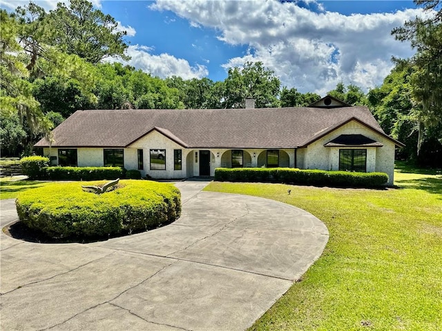 ranch-style house featuring a chimney, curved driveway, and a front lawn