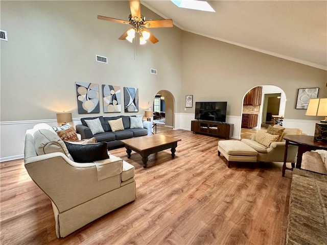 living area featuring wood finished floors, visible vents, wainscoting, ceiling fan, and arched walkways