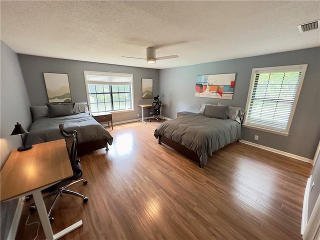 bedroom with baseboards, visible vents, a textured ceiling, and wood finished floors