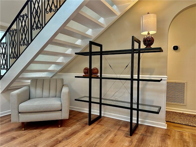 sitting room featuring stairway, arched walkways, baseboards, and wood finished floors